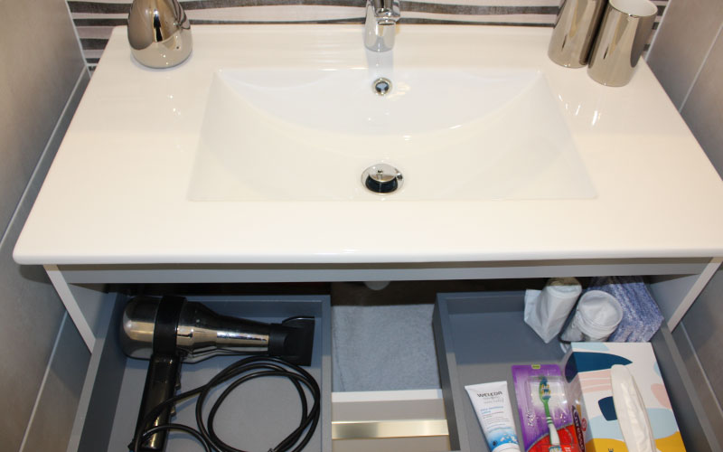 Photo du lavabo de la salle de bain où l'on voit un sèche-cheveux et des produits du quotidien
