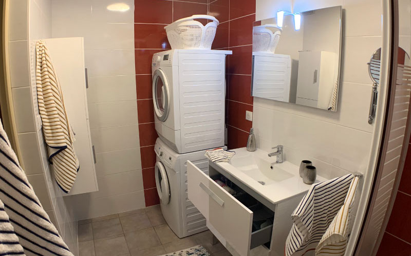 Photo de la salle de bain où l'on voit le lavabo, le lave-linge, le sèche-linge